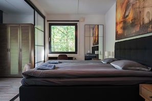 Une chambre moderne avec un grand lit, un bureau et une fenêtre donnant sur un paysage verdoyant.