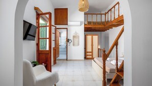 Une pièce spacieuse avec un escalier en bois, un téléviseur à écran plat fixé au mur et un coin salon confortable avec un fauteuil et une petite table.