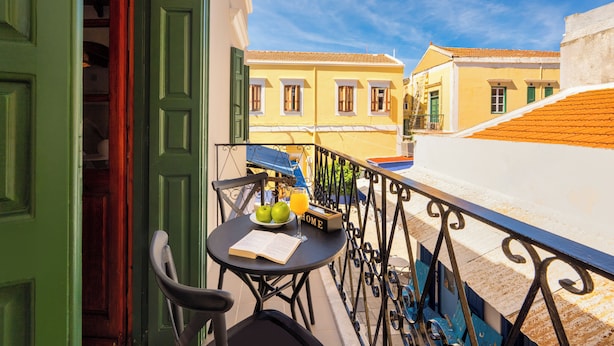 Un balcon avec une table, une chaise, un livre, une assiette de pommes et un verre de jus d’orange.
