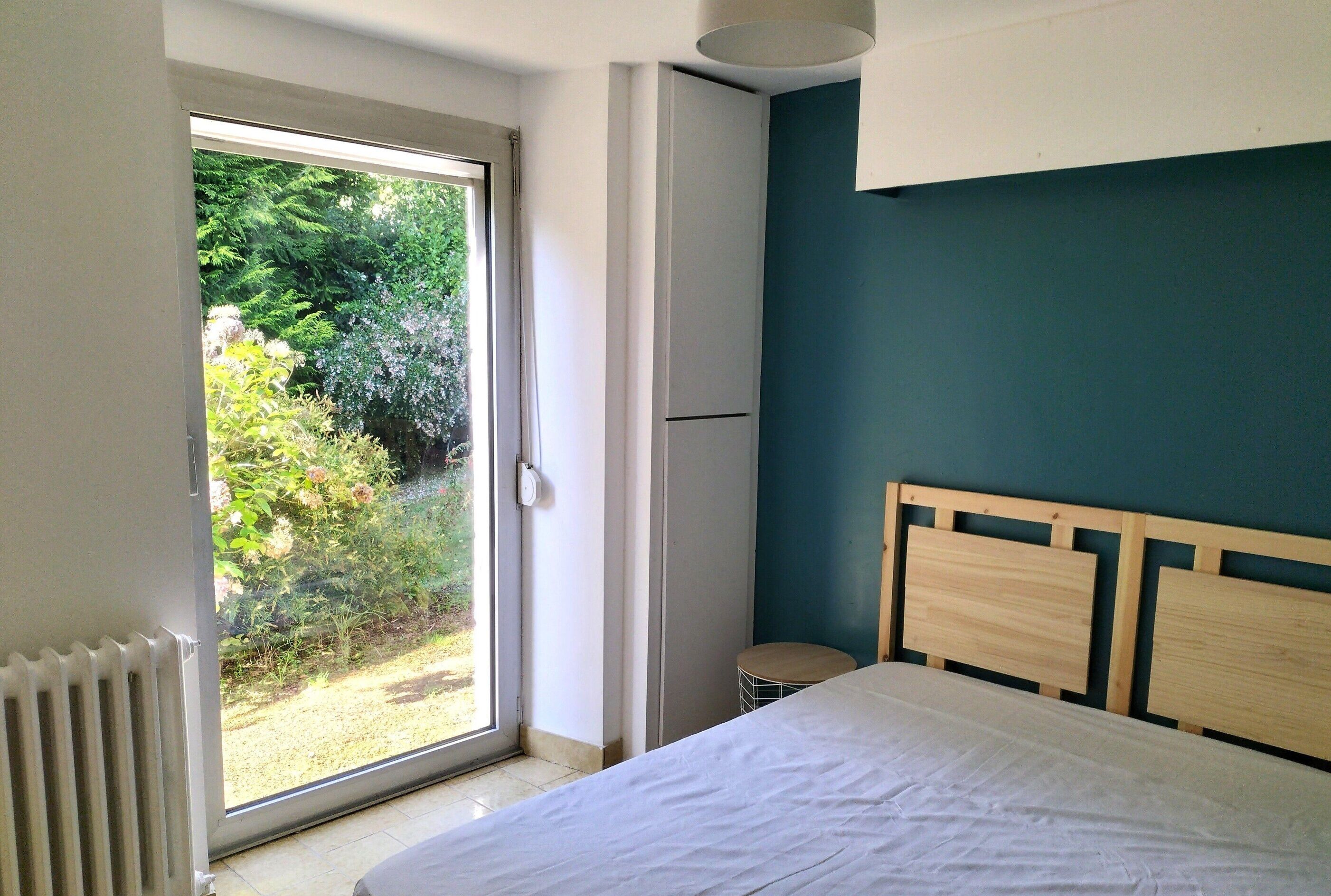 A bedroom with a large window, a bed, and a wooden headboard.