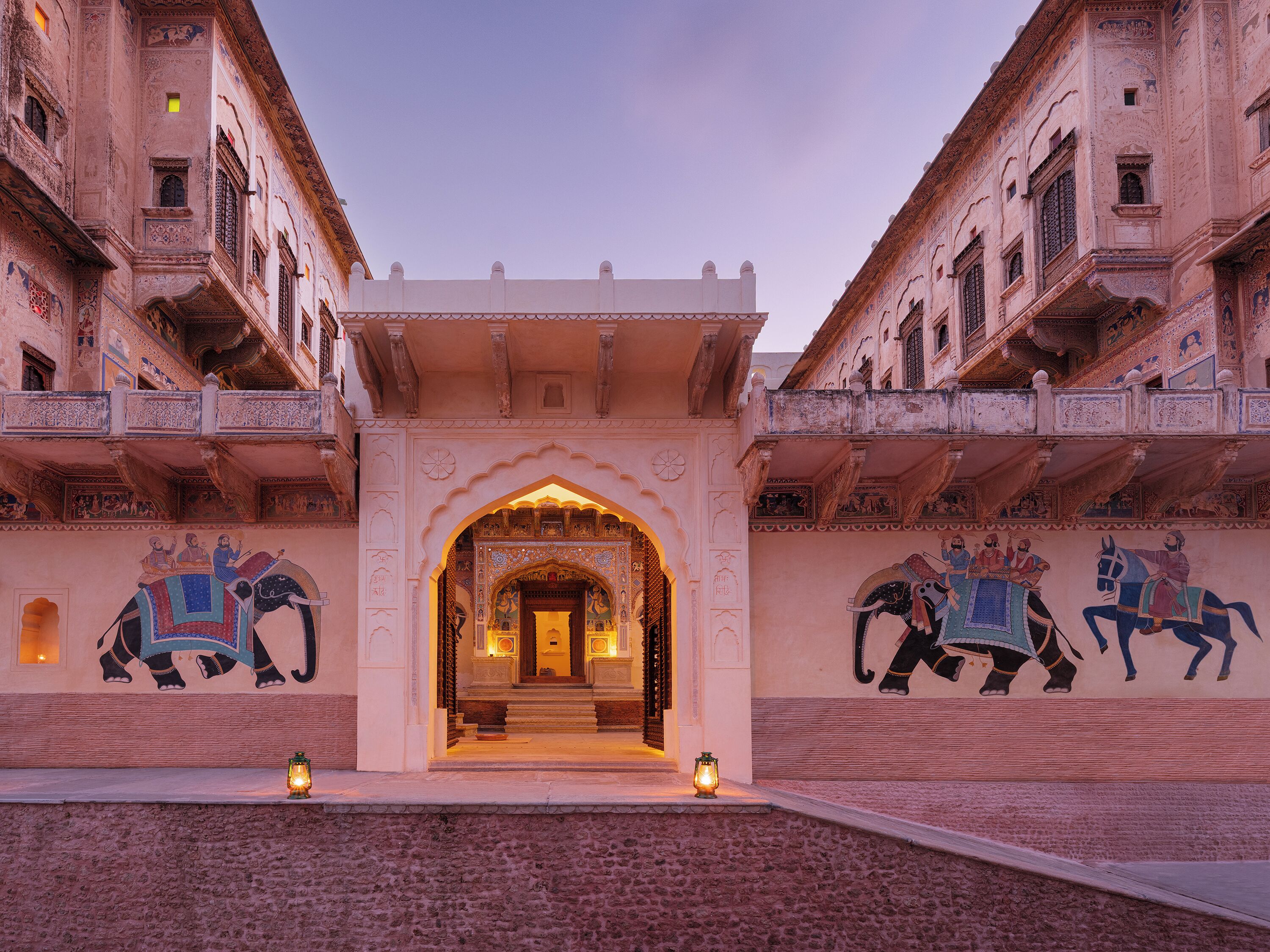 Een statig entree met ingewikkelde snijwerken en een centrale boogpartij, omlijst door muurschilderingen van olifanten en ruiters.