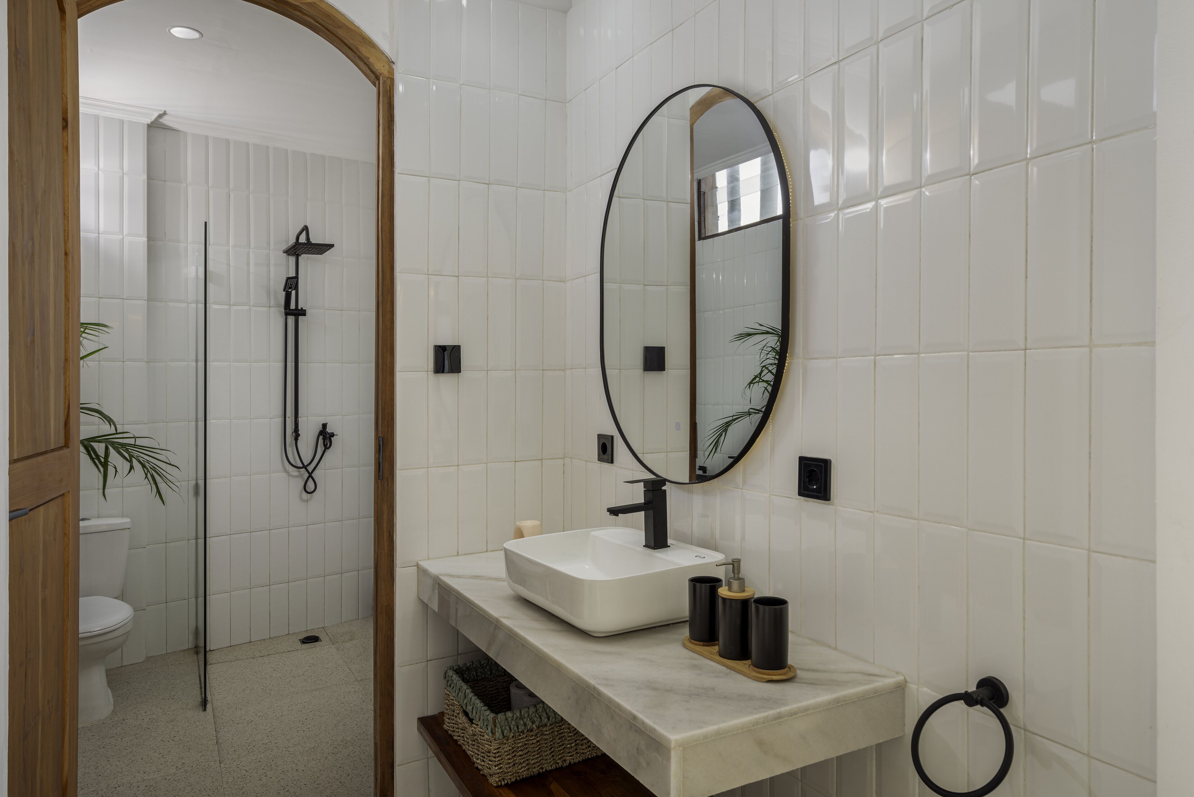 A bathroom with a white tiled wall, a rectangular sink with a black faucet, a mirror with a black frame, and a towel ring.