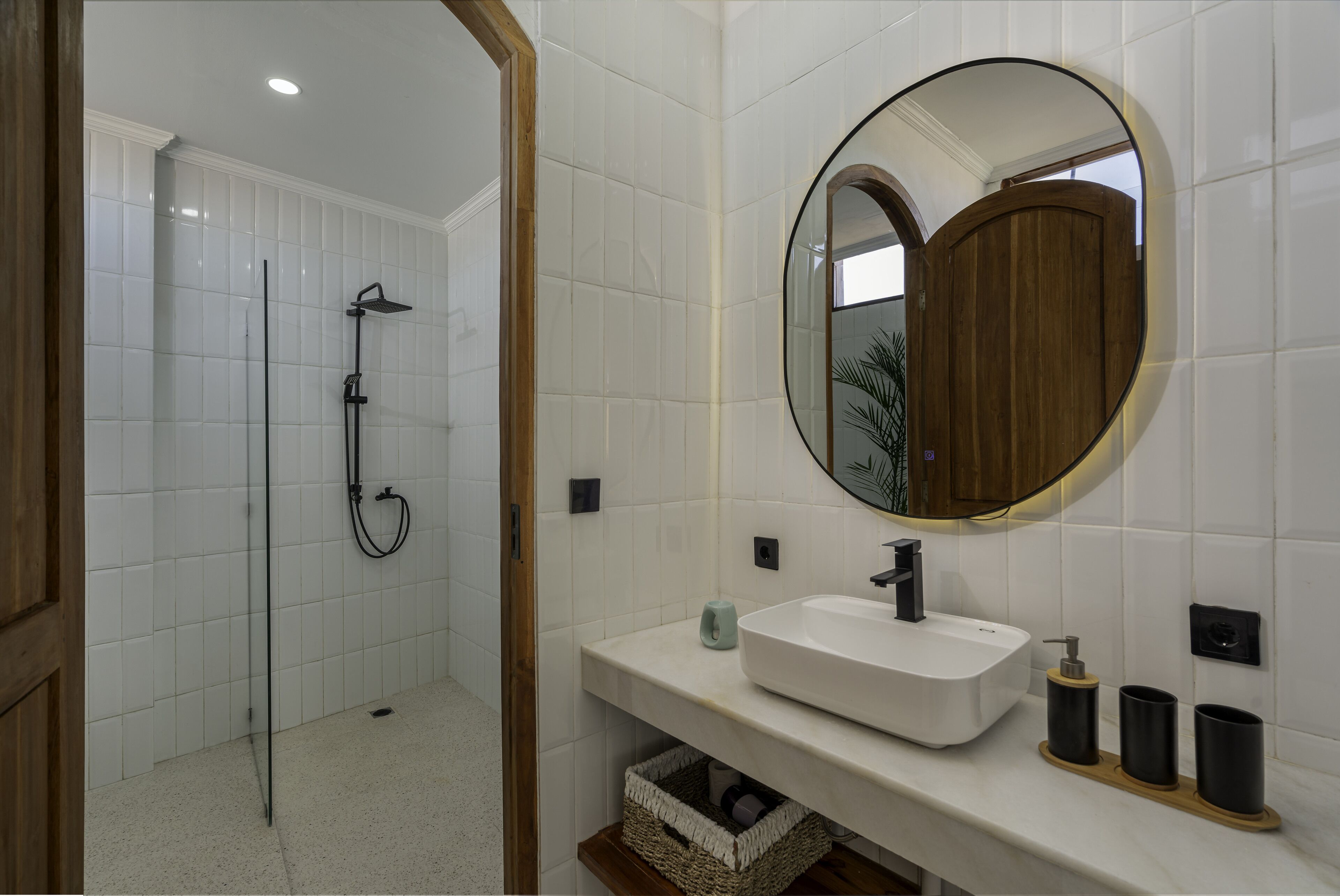 A bathroom with a white tiled shower, a wooden-framed mirror, and a white sink with black fixtures.
