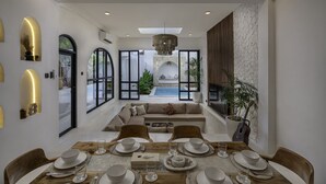 A modern dining area with a large table set for six, a sofa in the background, and a view of a pool and outdoor space.