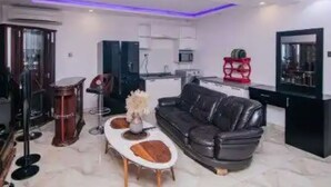 A modern living room with a black leather sofa, a white coffee table, and a dining area with a red chair. - Appleville Suites (Lagos)