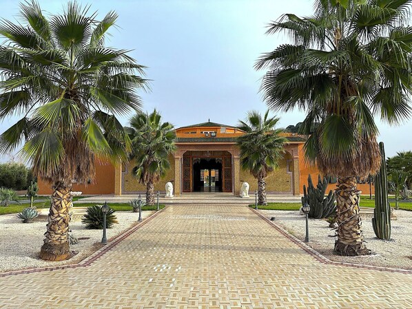 A building with a tiled entrance, surrounded by palm trees and cacti.
