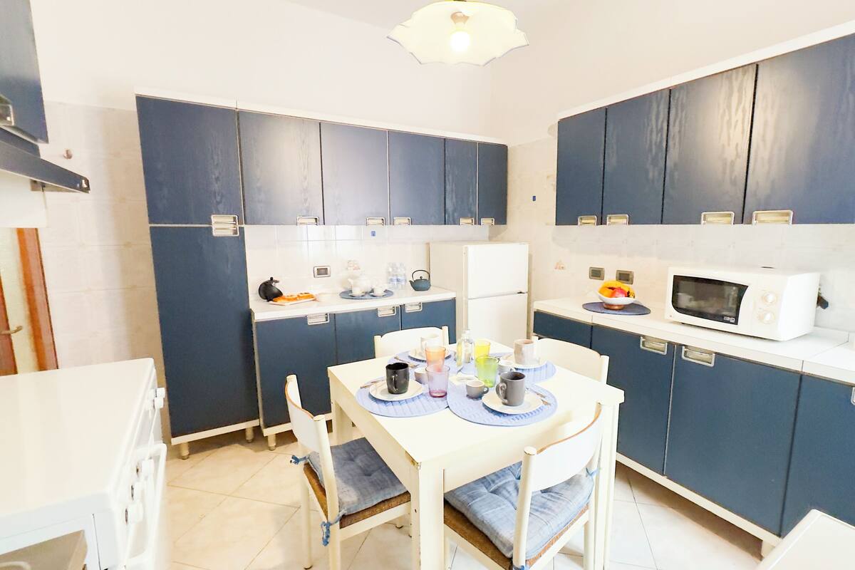 A compact kitchen with dark blue cabinets, a white countertop, and a dining area with a table and chairs.