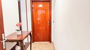 Una porta di legno con una maniglia, un vaso bianco con fiori rosa su un tavolo di legno e un pavimento piastrellato.