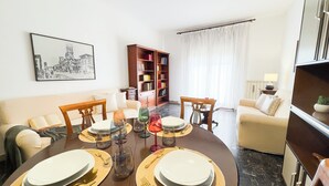 Zona pranzo con tavolo rotondo apparecchiato per quattro persone, circondata da divani e una libreria.