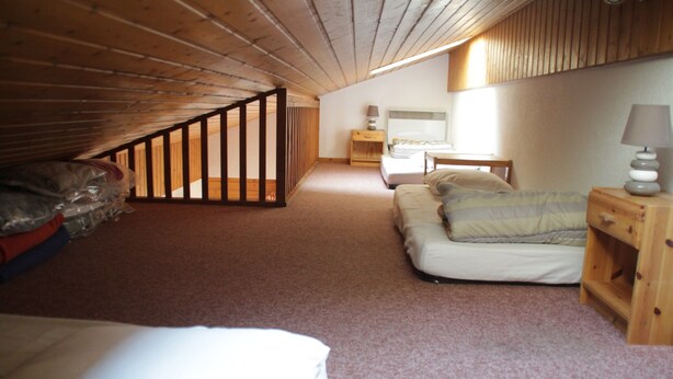 A small, cozy attic bedroom with a sloped ceiling, a wooden staircase, a bed, a nightstand, and a lamp. - Voinettes Vnb7 Telecabine & Mountain 5 Pers (Chatel)