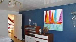 A bedroom with a bed, a dresser, a desk, and a wall with a colorful painting. - Cap sur le Sable at Port de Moguériec (Sibiril)