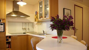 A kitchen with wooden cabinets, a stainless steel range hood, a white countertop, and a vase with purple flowers on the table. - Cap sur le Sable at Port de Moguériec (Sibiril)