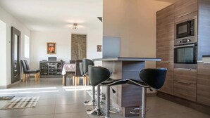 A modern kitchen with built-in appliances, a dining area with a table and chairs, and a bar area with stools.