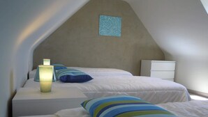A bedroom with two beds, a nightstand, a lamp, and a small window.