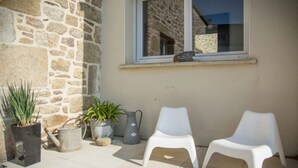 A patio with two white plastic chairs, a stone wall, and potted plants.