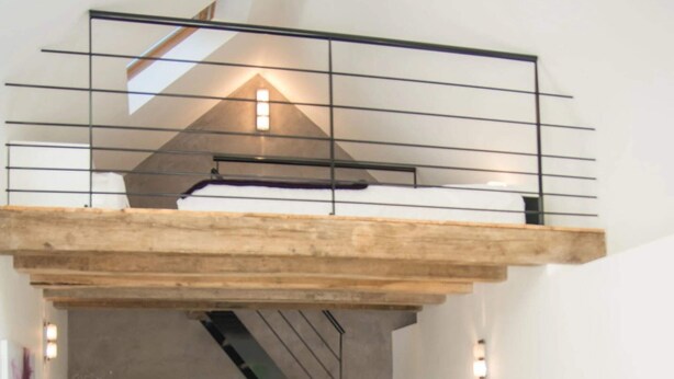 A loft-style living room with a high ceiling, a staircase, a flat-screen TV, a sofa, and a coffee table.