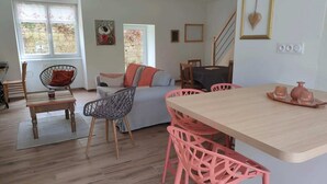A cozy living room with a wooden dining table, pink chairs, a grey sofa, and a small kitchen area with a window. - Le Guillec in the heart of the Valley (Sibiril)