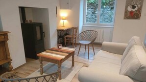 A living room with a sofa, a wooden coffee table, a chair, a lamp, and a view of a stone wall through a window. - Le Guillec in the heart of the Valley (Sibiril)