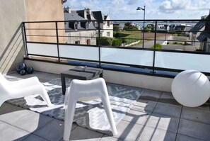 Un balcon doté d’une rambarde en métal, deux chaises en plastique blanc, une petite table ronde et un objet sphérique blanc.