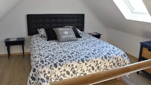 Een slaapkamer met een schuine plafond, een bed met een bloemenprint sprei, twee nachtkastjes en een bijzettafeltje.