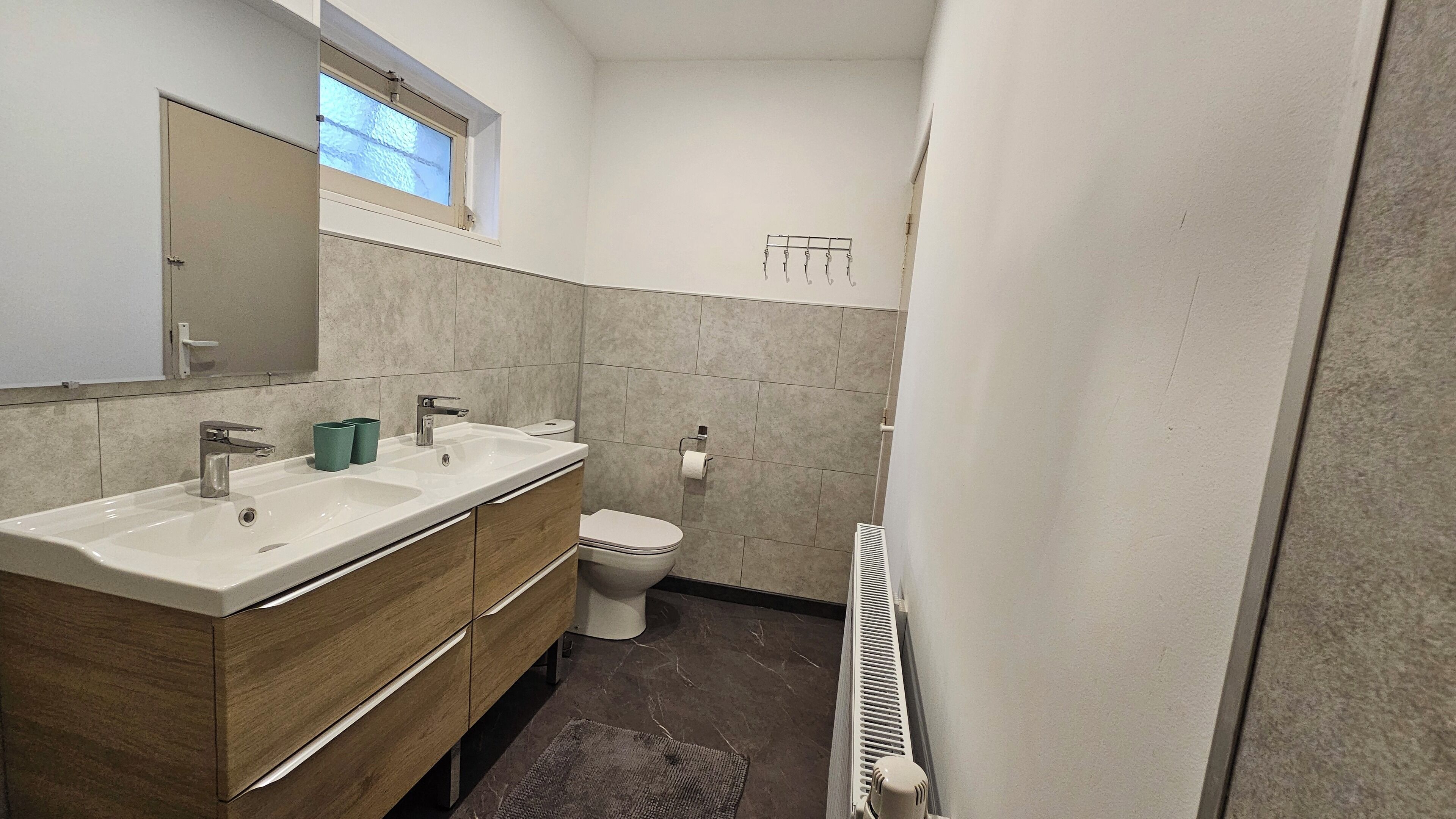 Une petite salle de bain comprenant un lavabo double, un meuble-lavabo en bois, des toilettes et un radiateur.