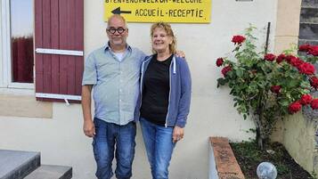 A couple standing in front of a building with a sign indicating camping and gîtes, welcoming visitors.