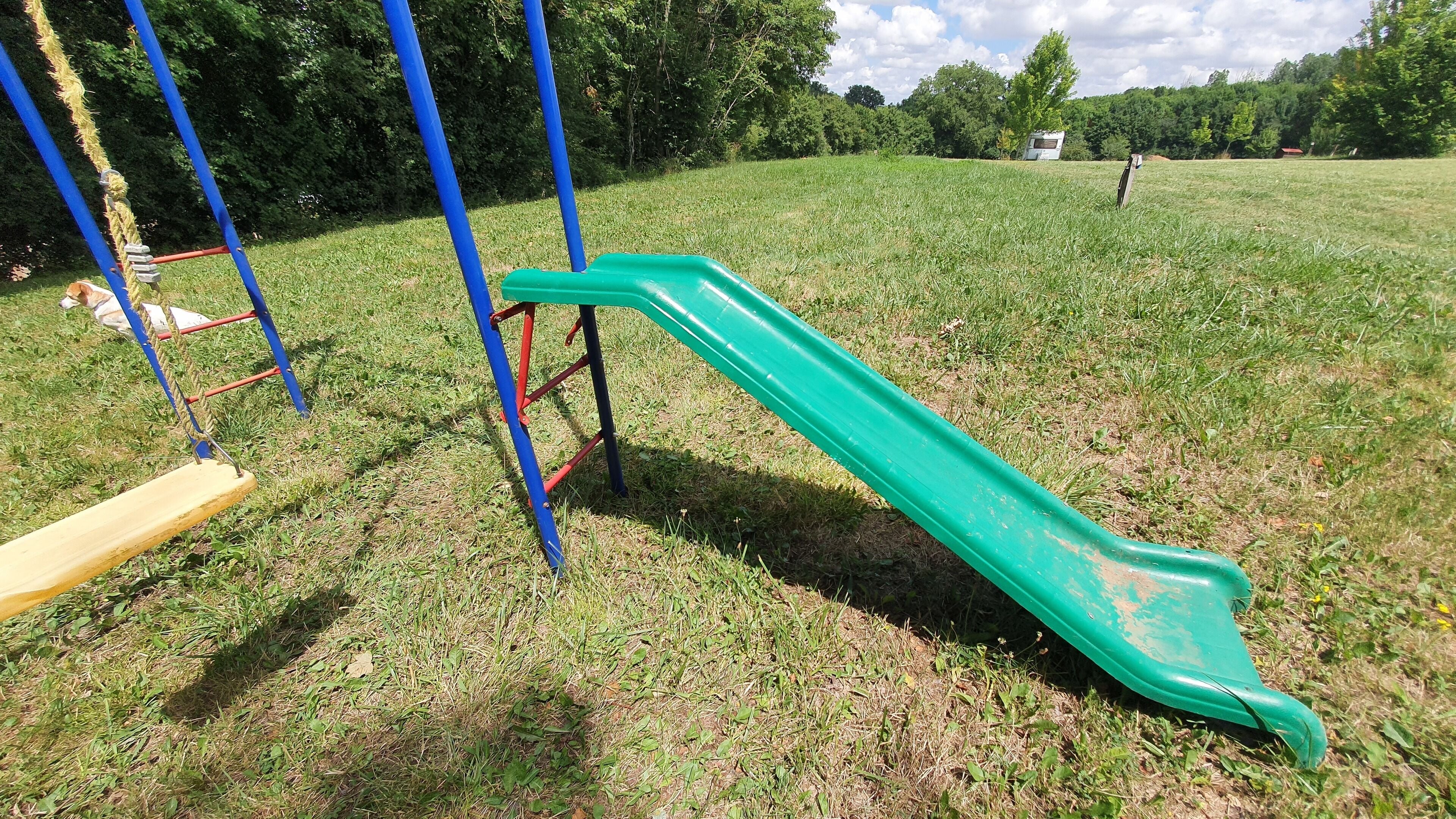 Een speeltuin met een groene glijbaan en een gele schommel in een grasveld.