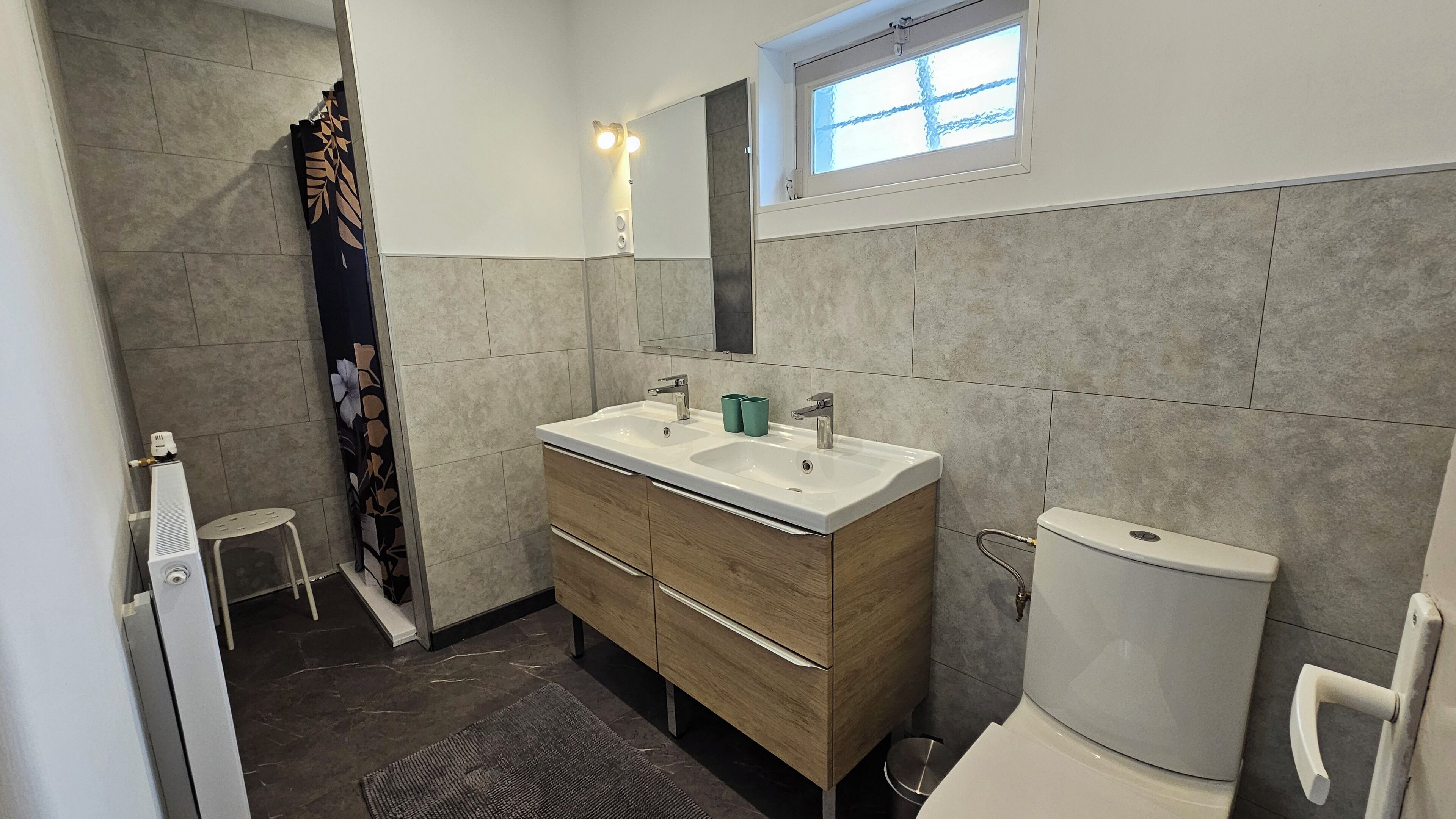 Een moderne badkamer met twee wastafels, toilet, raam en douche.