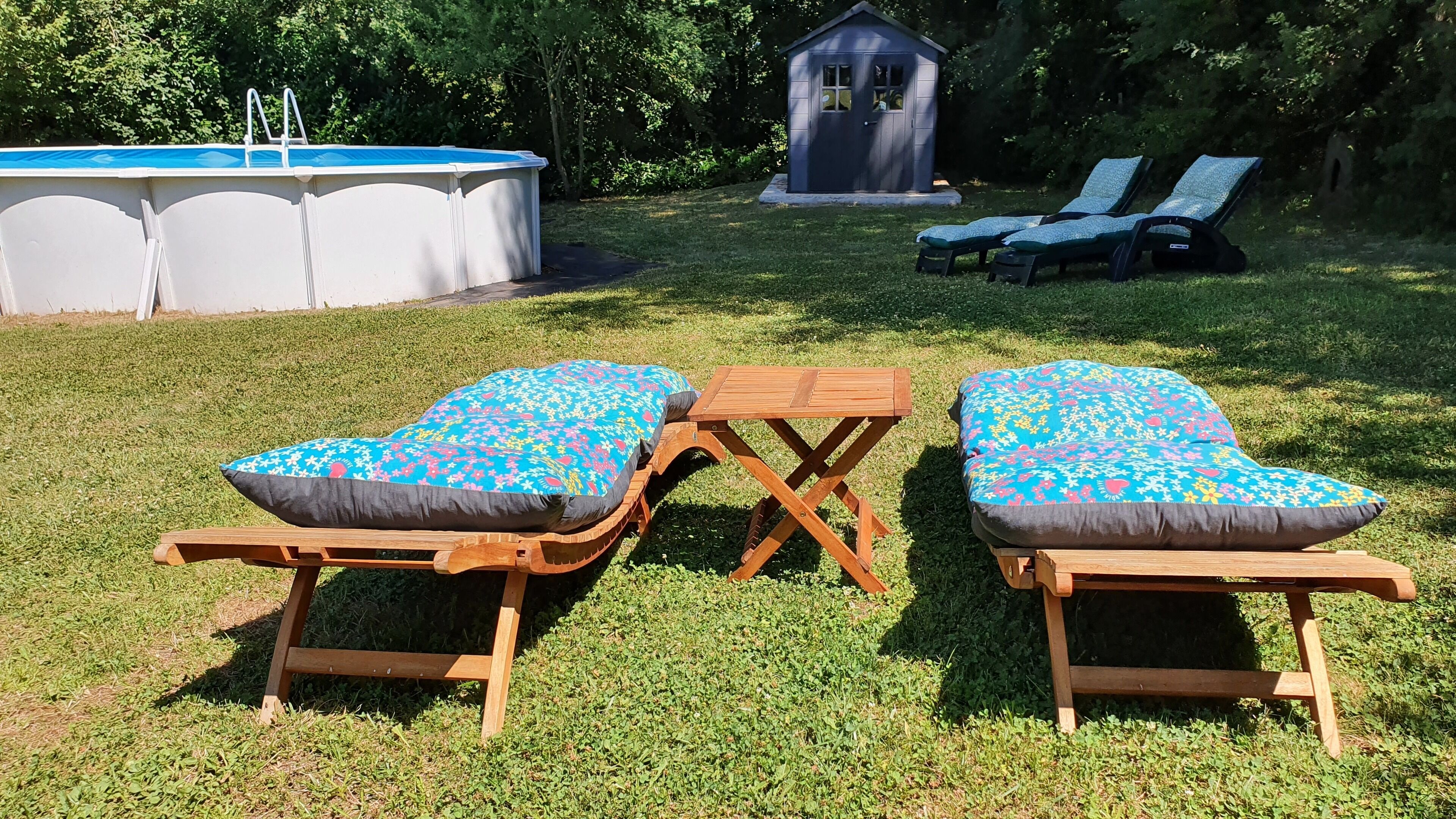 An outdoor pool area with two wooden lounge chairs and a small wooden table.