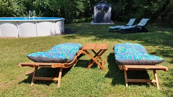 An outdoor pool area with two wooden lounge chairs and a small wooden table.