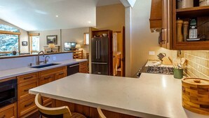 A modern kitchen with wooden cabinets, a stainless steel refrigerator, and a large island with a sink. - Gore Creek Alpine Chalet (Vail)