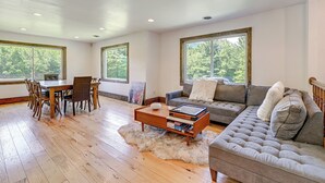 A spacious living room with a wooden dining table, a grey sofa, and a fluffy rug. - 3 Mi to Colgate Lake: Mtn-view Home, Deck + Grill! (East Jewett)