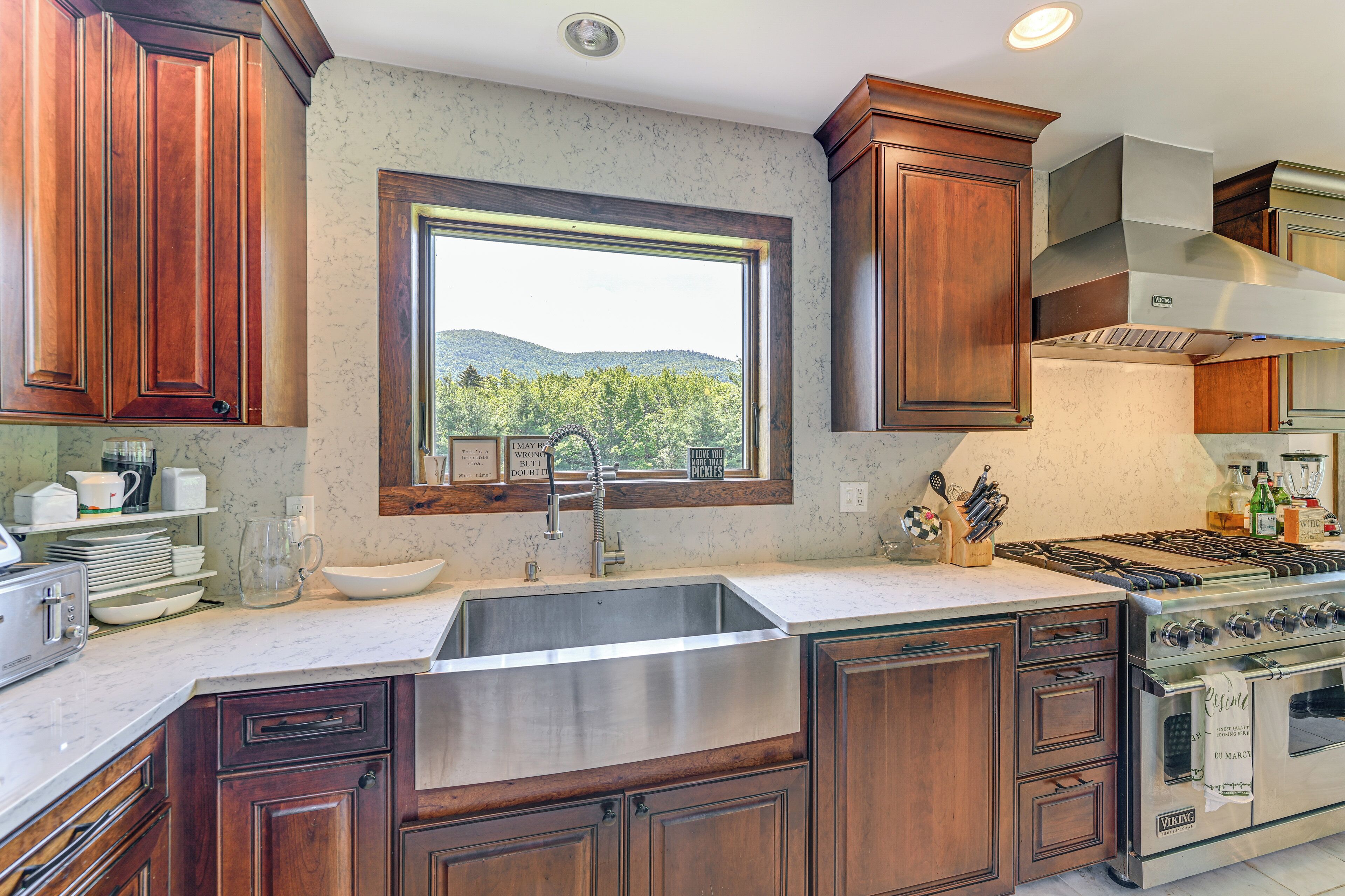 A kitchen with wooden cabinets, a stainless steel sink, a window with a view of greenery, and a Viking stove.