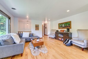 A modern living room with a grey sofa, a wooden coffee table, and a grey armchair. There is a bookshelf with books and decorative items, and a painting on the wall. - 3 Mi to Colgate Lake: Mtn-view Home, Deck + Grill! (East Jewett)