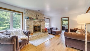 A spacious living room with a stone fireplace, two sofas, and a large window offering a view of trees. - 3 Mi to Colgate Lake: Mtn-view Home, Deck + Grill! (East Jewett)