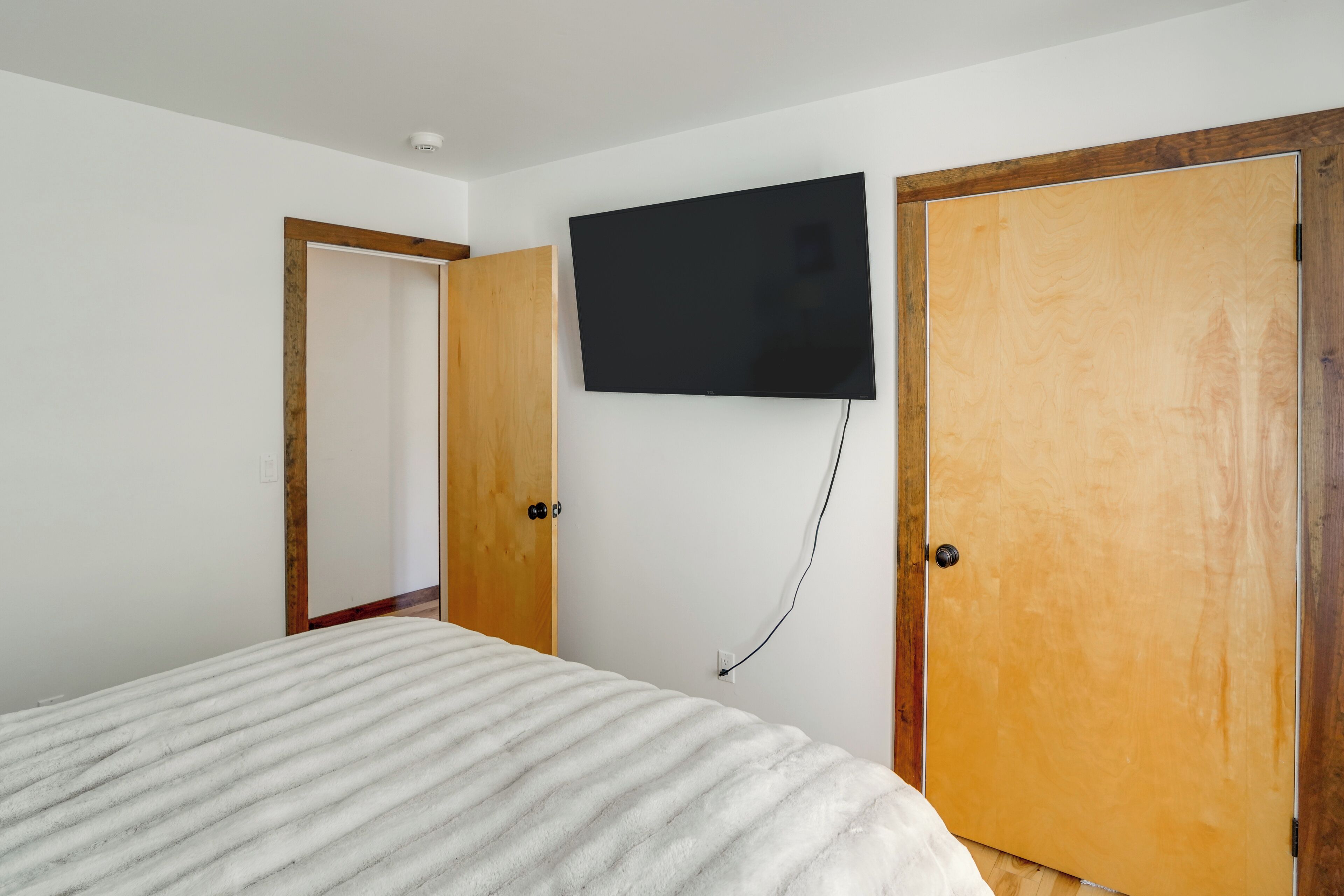 A bedroom with a bed, a wooden door, and a mounted TV.