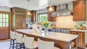 A kitchen with wooden cabinets, a large island with bar stools, a stove, and a window overlooking greenery. - 3 Mi to Colgate Lake: Mtn-view Home, Deck + Grill! (East Jewett)