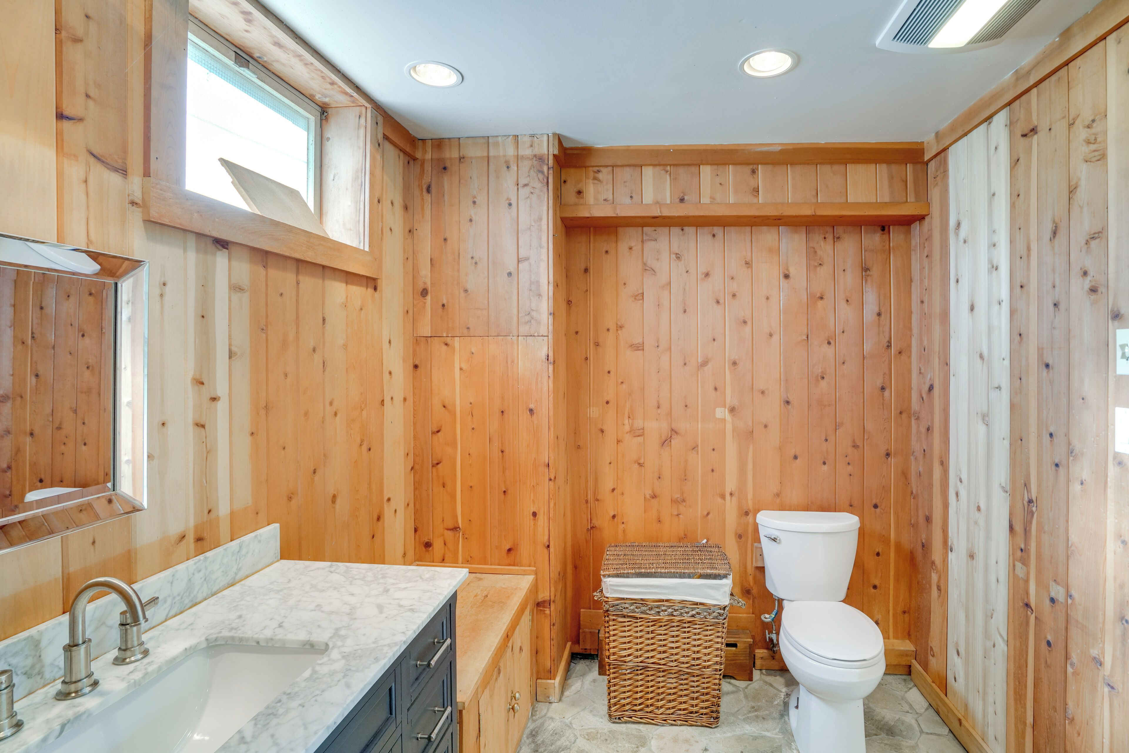 A wooden-paneled bathroom with a marble sink, a toilet, and a wicker basket.