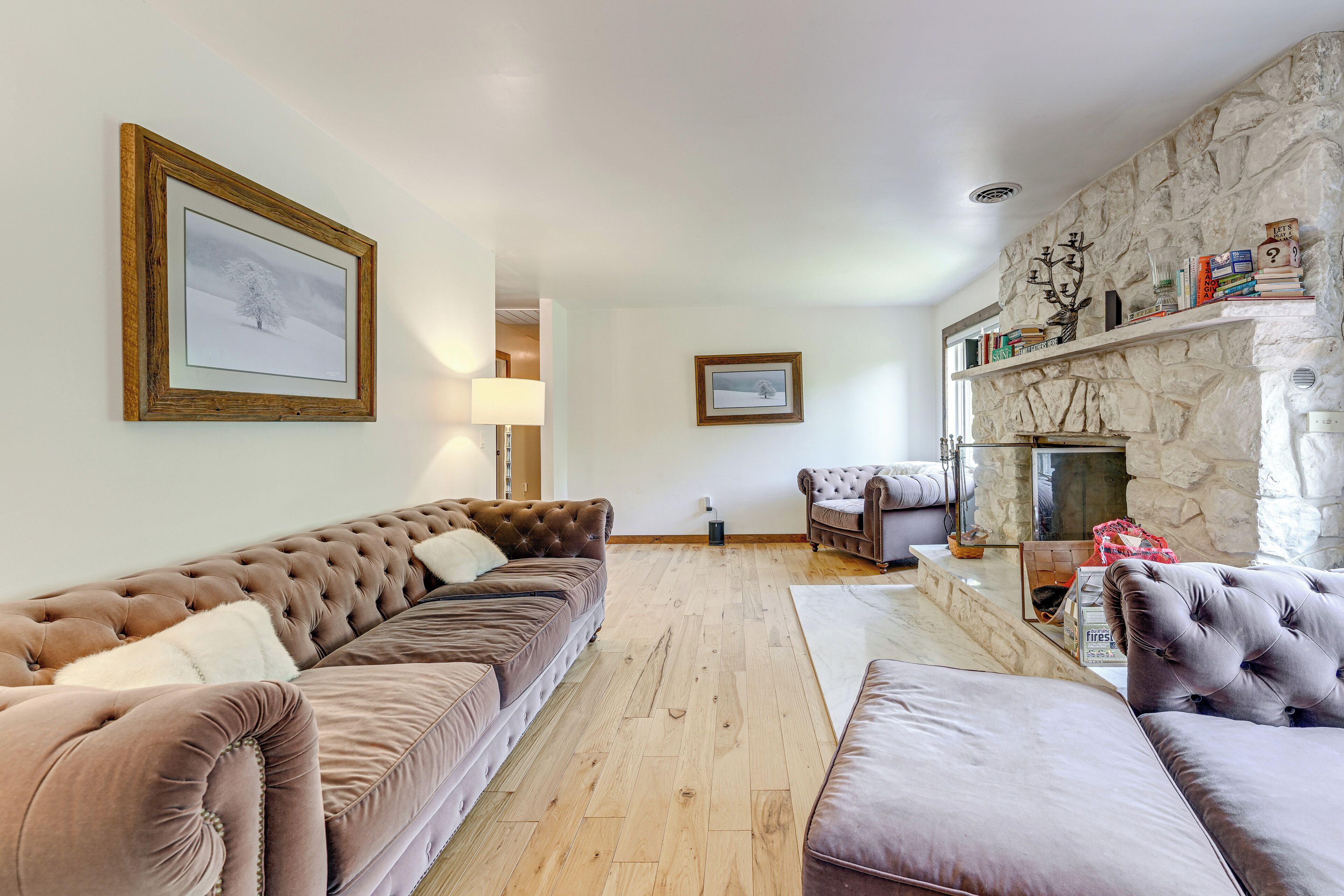 Un salon avec un canapé marron, un fauteuil gris, une cheminée et un mur en pierre.