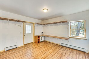 Habitación con piso de madera, un banco integrado, un calentador, una puerta y una ventana con vista a árboles.