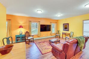 Una sala de estar con piso de madera, un sofá de cuero marrón, una mesa de centro de madera, un mueble de color turquesa y un televisor.