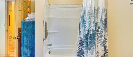 Un baño con bañera, cortina de ducha con diseño de bosque y puerta de madera.