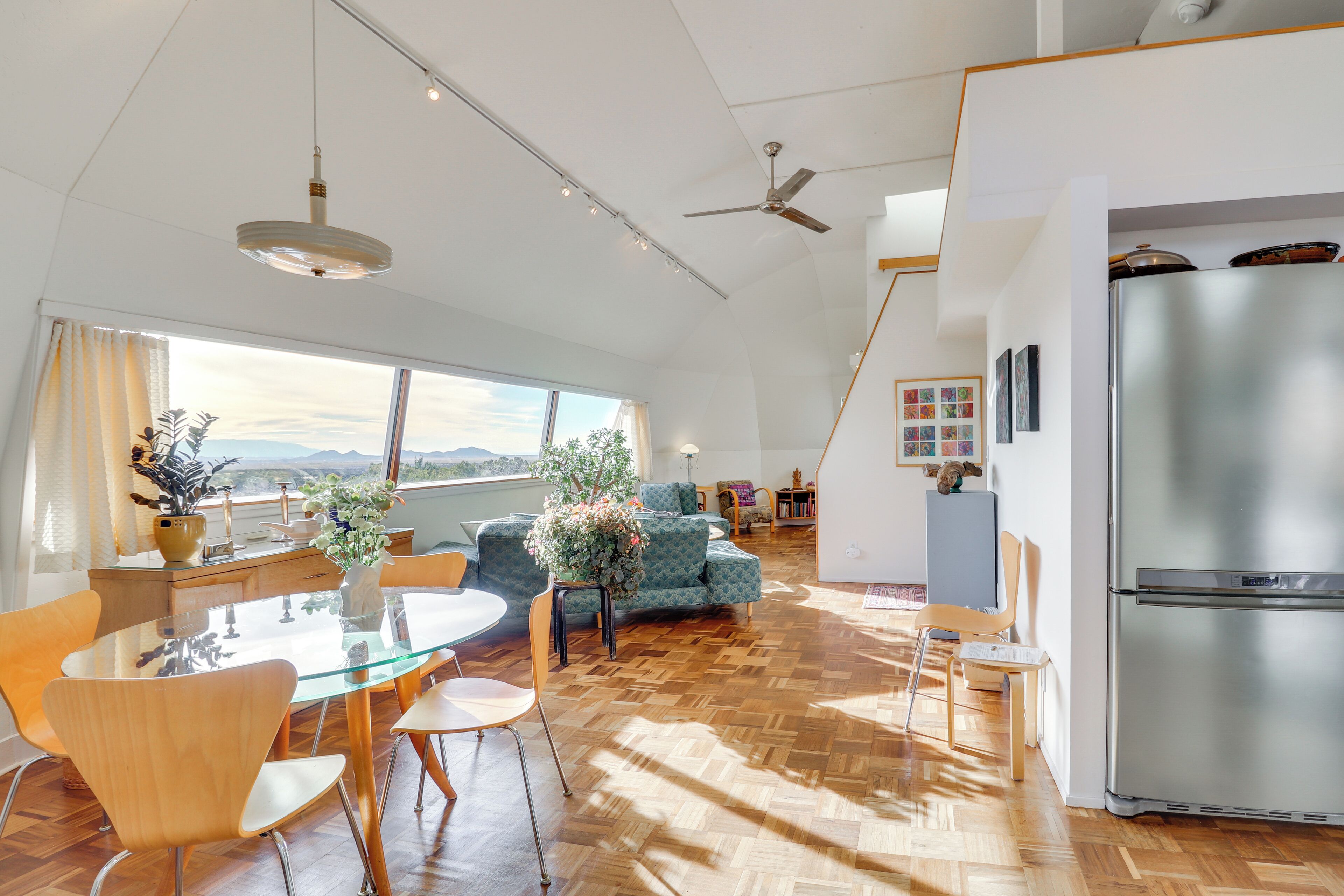 A modern kitchen with a large refrigerator, wooden flooring, and a dining area with a glass table and chairs.
