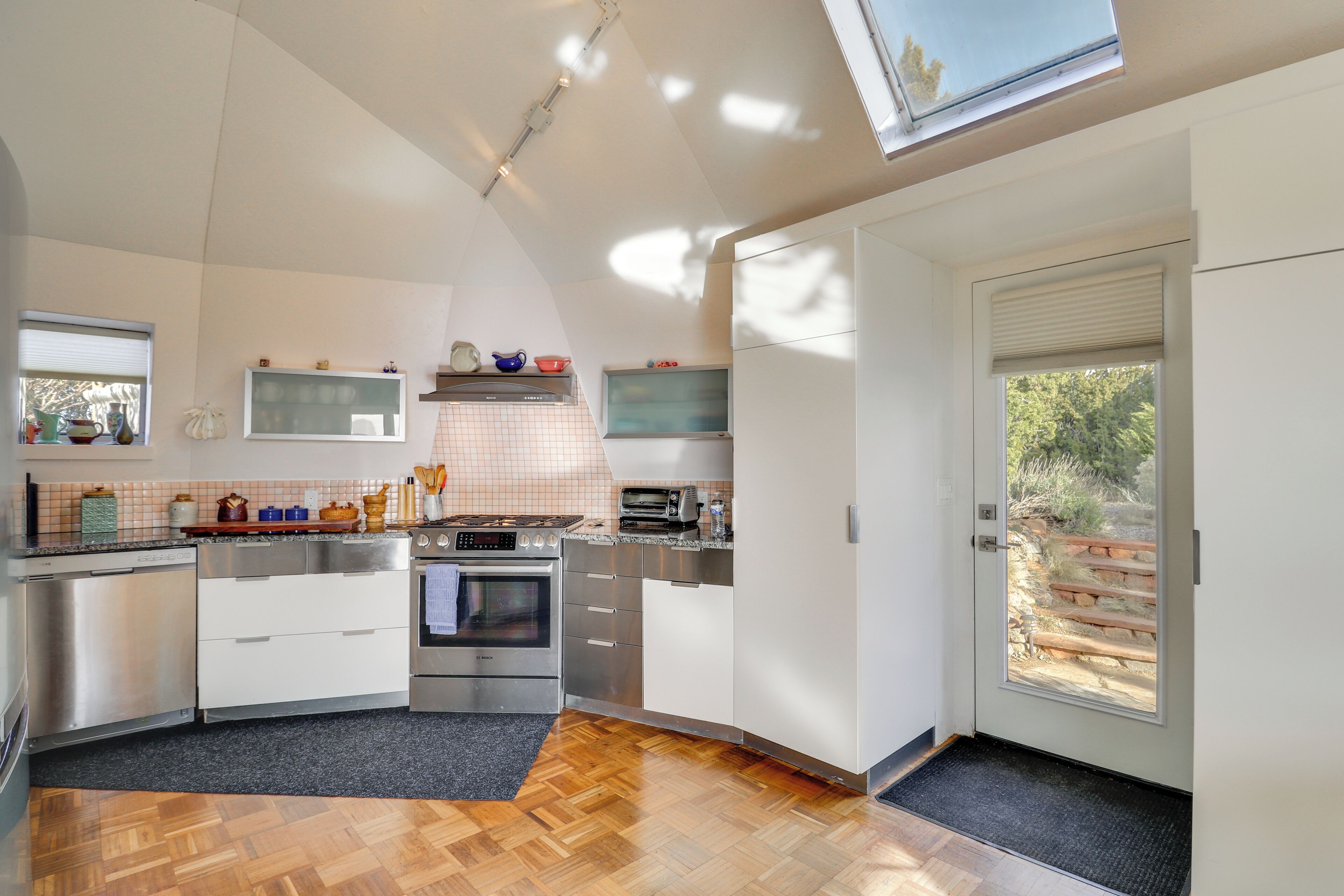 A modern kitchen with stainless steel appliances, a wooden floor, and a skylight.