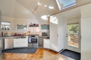 A modern kitchen with stainless steel appliances, a wooden floor, and a skylight.