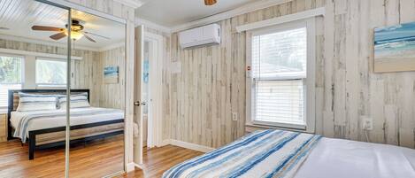 A bedroom with a wooden floor, a bed with a striped blanket, a ceiling fan, and a window with blinds.