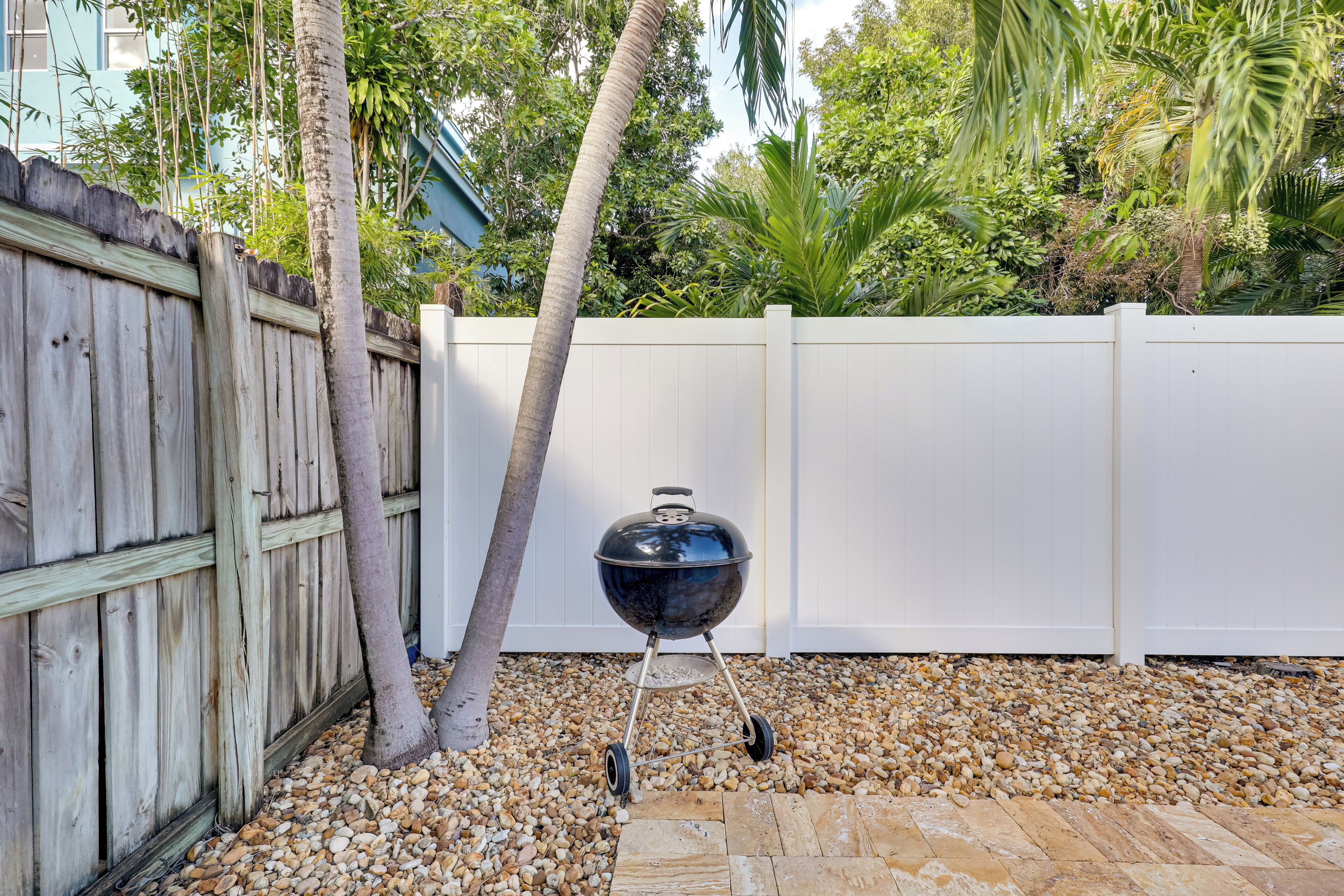 A barbecue grill in a backyard with a wooden fence and palm trees.