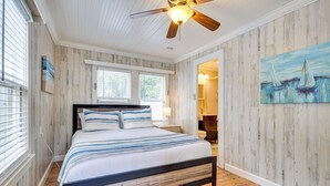 Een slaapkamer met een plafondventilator van hout, een bed met gestreepte beddengoed, en een schilderij van zeilboten aan de muur.