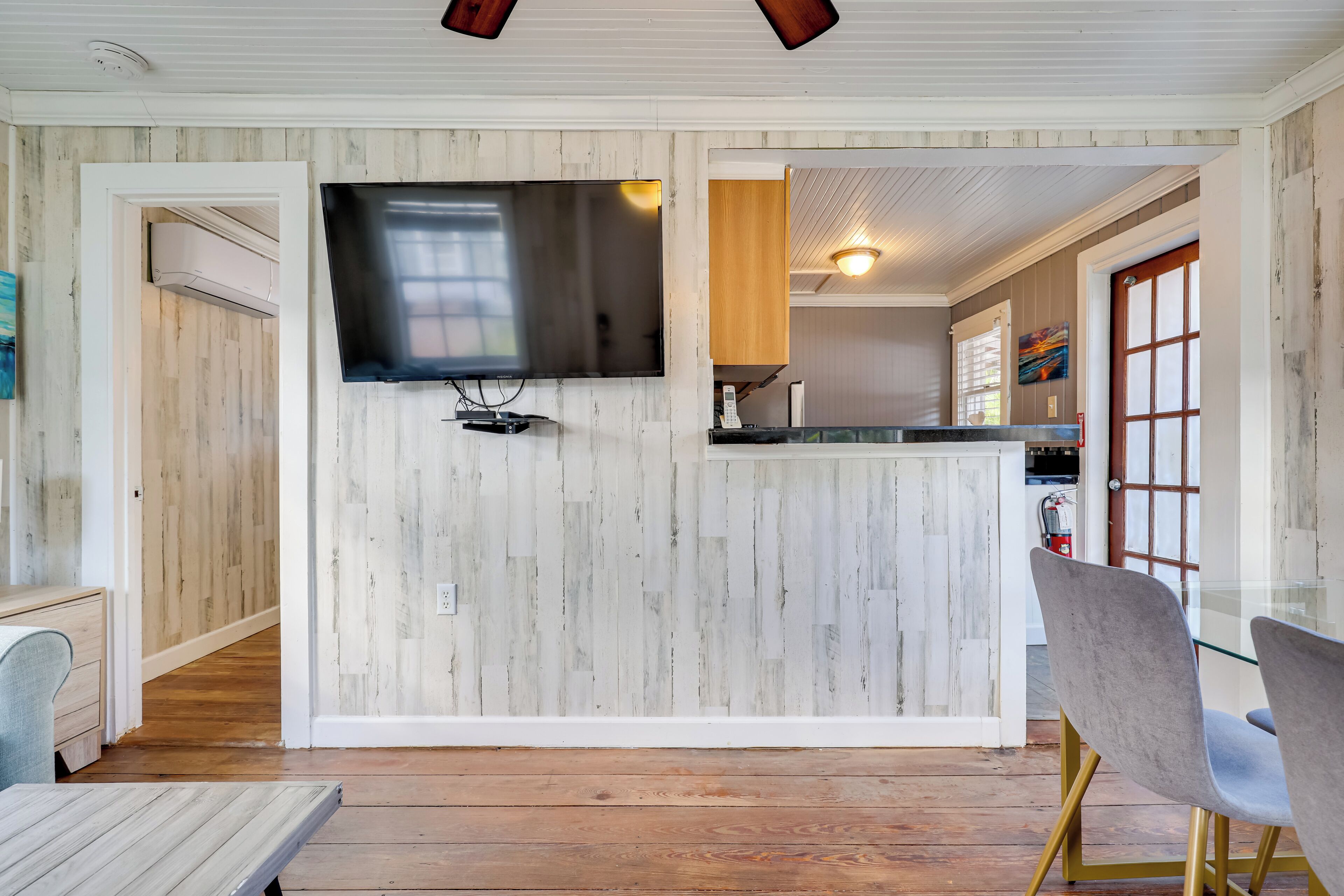 A modern kitchen with a flat-screen TV, wooden walls, and a glass dining table with chairs.