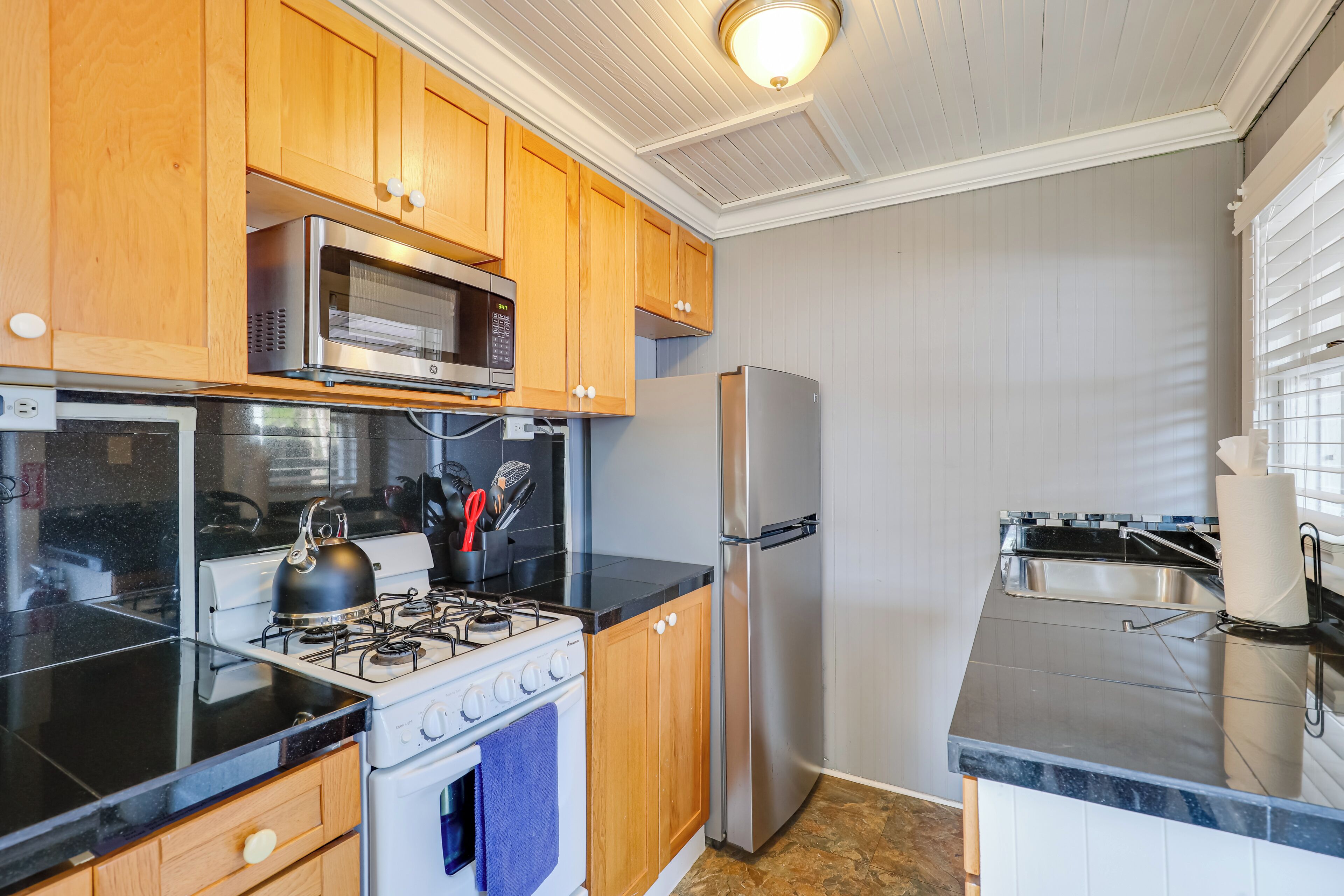 A kitchen with wooden cabinets, a stainless steel refrigerator, a microwave, a stove, and a sink.